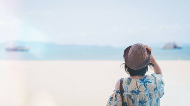 Plajda yaz tatili kavramı. Mutlu bir kadın, şapkasını takıp, sahilde dinleniyor ve yazın bir yolcu gemisinin arka planına ve deniz sahiline bakıyor..