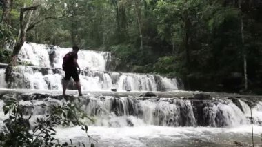 Sırt çantalı gezgin, inanılmaz tropikal şelalenin keyfini çıkarıyor. El kaldırıyor, seyahat ediyor ve tatil kavramını başarıyor.