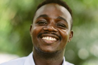 Afrikalı adam açıkça gülümsüyor. Beyaz gömlekli siyah adam, dişlerini göstererek gülümsüyor..