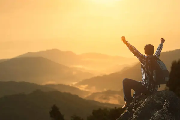 Sırt çantalı bir yürüyüşçü bir dağ zirvesini fethetmek için gururla elini kaldırır. Gezgin, kollarını açmış, sisli yüksek bir dağın tepesinde başarıyı ve özgürlüğü iletmek için oturur.