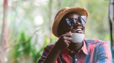 Güneş gözlüğü takan Afrikalı turist sabahları sıcak kahve içiyor.