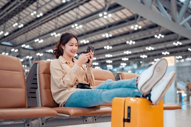 Mutlu Asyalı turist kadın cep telefonu kullanıyor ve bavulunu bavula koyuyor. Havalimanı Terminali 'nde uçuş, internet taraması, uçuş kontrolü, turist yolculuğu konsepti arasında seyahat ediyor.