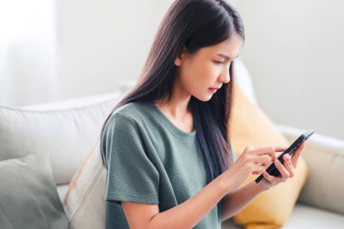 Akıllı telefon ekranına bakan endişeli genç bir kadın, kötü haber, spam veya dolandırıcılık mesajlarından memnun değil. Kötü ruh hali yaşam tarzı konsepti.