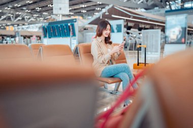 Havalimanı Terminali 'nde uçuş, internet, uçuş kontrolü, turist yolculuğu konsepti arasında seyahat eden cep telefonu kullanan mutlu Asyalı turist kadın.