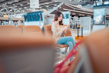 Havalimanı Terminali 'nde uçuş, internet, uçuş kontrolü, turist yolculuğu konsepti arasında seyahat eden cep telefonu kullanan mutlu Asyalı turist kadın.