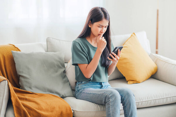 Worried young woman looking at smartphone screen, dissatisfied with bad news message, spam or scam sms. Bad mood lifestyle concept.