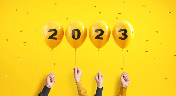 New year number 2023 of balloons in hands with confetti on yellow background.