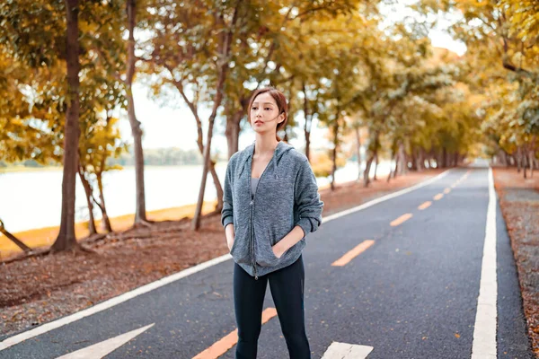 Asian woman in hoodie running sport exercises outdoors on a background of park trees on autumn day. Healthy lifestyle well being wellness happiness concept