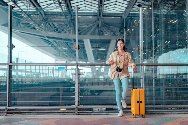 stock image Happy attractive asian woman passenger traveler with a yellow suitcase at the modern airport terminal, copy space, Tourist journey trip concept