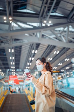 Happy attractive asian woman traveler with mask at the modern airport terminal, copy space, Tourist journey trip concept