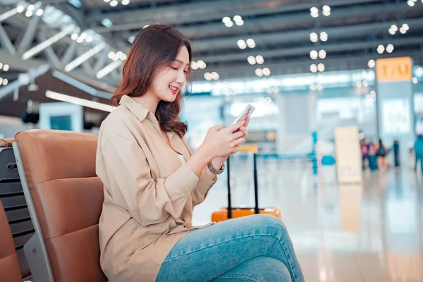 stock image Happy asian tourist woman passenger using mobile smartphone with suitcase traveling between waits for flight in Airport Terminal, Browse Internet, flight check in, Tourist journey trip concept