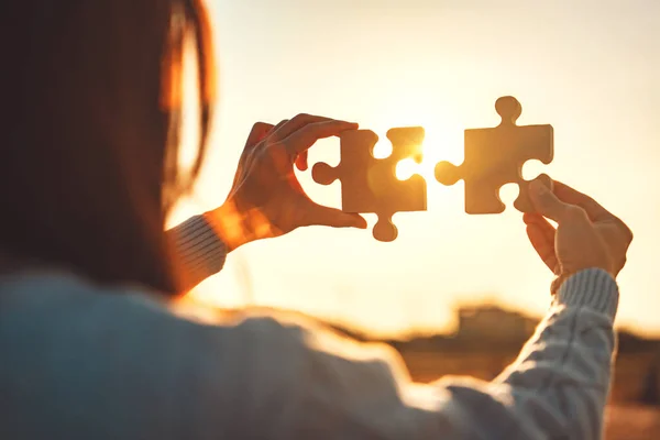 Closeup hands of woman connecting jigsaw puzzle with sunlight effect, Jigsaw alone wooden puzzle against sunset, Business solutions, Success and strategy concept