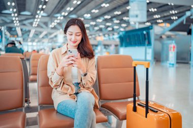 Havalimanı Terminali 'nde uçuş, internet gezisi, uçuş kontrolü, seyahat konsepti arasında seyahat eden cep telefonu kullanan mutlu Asyalı turist kadın.
