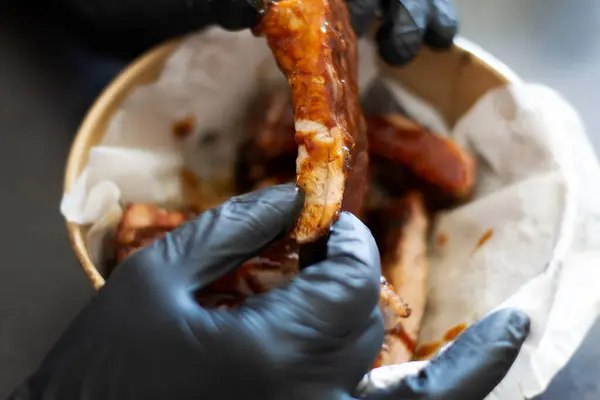 Izgara lokantası yemek teslimatı. Siyah eldivenli bir adam elinde karikatür tabağındaki barbekü soslu domuz pirzolası tutuyor..