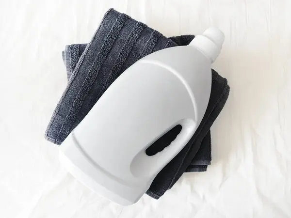 Temiz siyah havluların üzerine konmuş beyaz plastik deterjan kabı beyaz pamuk yüzeyine konmuş.