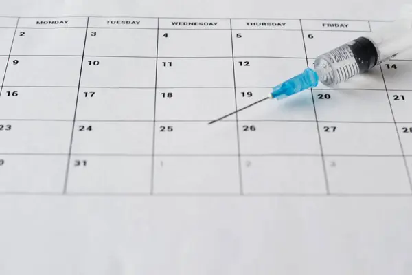 Beyaz takvim arka planında şeffaf aşı olan tıbbi şırınga. Kopya alanı ile aşılama takvimi kavramı