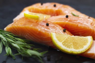 Taze somon dilimleri, biberiye, limon ve biber koyu dokulu masa.