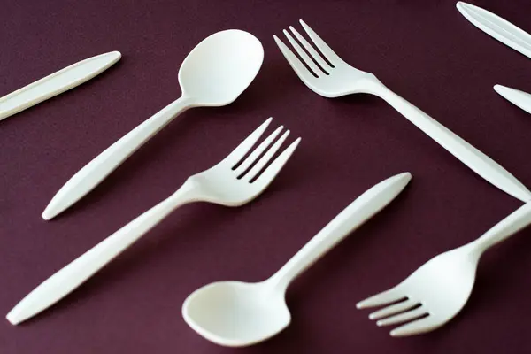 Renkli pembe menekşe arka planda beyaz plastik çatal ve kaşıklar, çevre dostu.