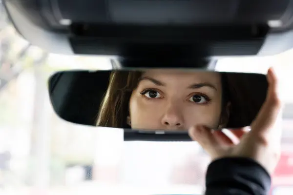 Sürücü koltuğunda oturan genç kadın arabasındaki dikiz aynasına bakıyor. Yaklaş.
