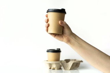 Beyaz arka planda plastik kapaklı, mukavva tutacağı olan, çevre dostu, biyolojik olarak çözünebilir, taklit edilebilen plastik kapaklı kadın eli kahve fincanları.