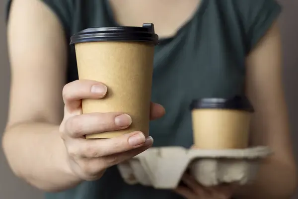 Elinde plastik kapaklı kağıt kahve fincanları ve karton tutacağı olan beyaz arka planda, çevre dostu, biyolojik olarak çözünebilir, model olan bir kadın.