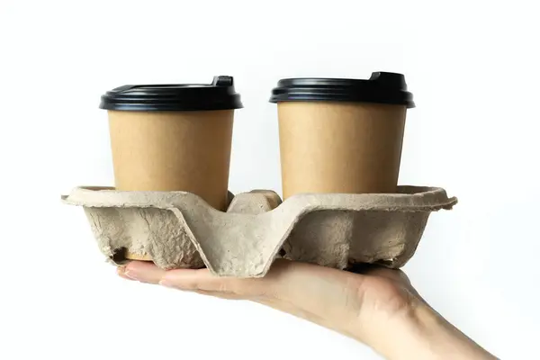 Beyaz arka planda plastik kapaklı, mukavva tutacağı olan, çevre dostu, biyolojik olarak çözünebilir, taklit edilebilen plastik kapaklı kadın eli kahve fincanları.