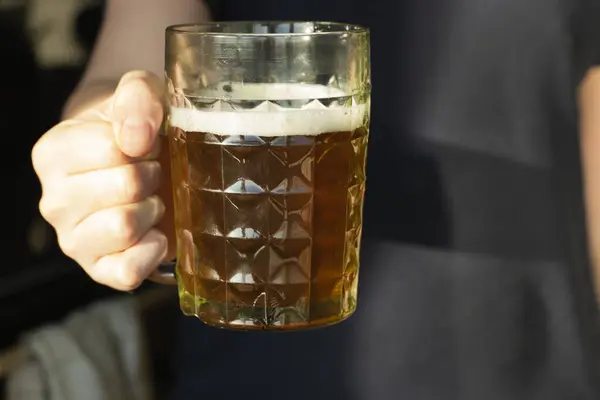 Adamın eli dolu bira bardağını tutuyor.