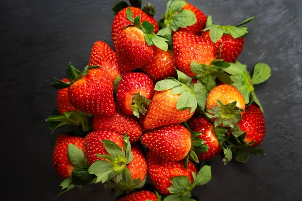 Siyah bir kasede taze, organik çilek, siyah bir levha, taş ya da beton zemin üzerinde. Kopyalama alanı olan üst görünüm.