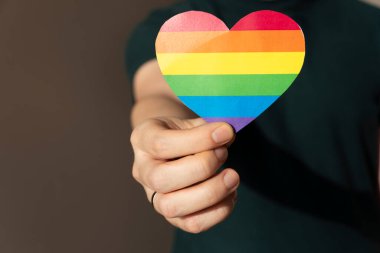 Kağıt kalpli LGBT bayrak renginde bir adamın yakın çekimi. Gay aşk konsepti