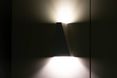 Aydınlatılmış bir modern geometrik duvar lambası. Yakın çekim, uzayda davetkar bir parıltı bırakıyor.