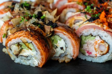 Siyah bir tahta üzerinde çeşitli suşi ruloları kremalı ve çıtır çıtır malzemelerle zarif bir ekranda dokuları ve renkleri birleştiriyor..