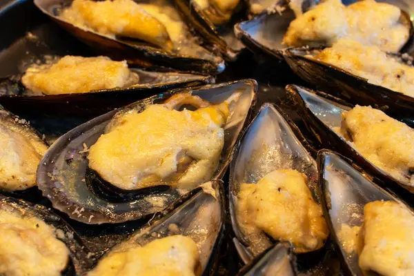 Kapalı kapılar ardında erimiş altın peynirle servis edilen kabuklu midyeler, tepside dizilmiş, lezzetli bir deniz ürünleri aperatifi, zengin ve lezzetli bir görünüme sahip..