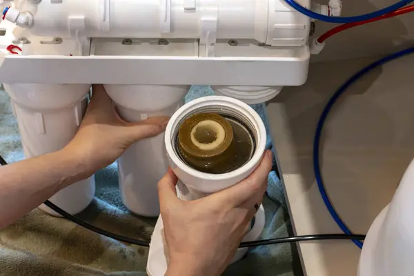 Ev yapımı osmoz su filtresi sisteminde bakım yapan bir kişi kirli kartuşlara erişmek için yuvanın vidalarını söker..
