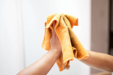 Female hand cleaning and wiping the mirror with orange microfiber cloth in the living room. Housekeeping concept.