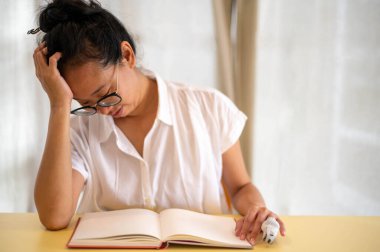 Genç Asyalı kadın odasında yalnız başına oturuyor, yüzü koyun ağlarken boş kitabı masaya koyuyor. Yalnızlık, stres ve endişe konsepti..