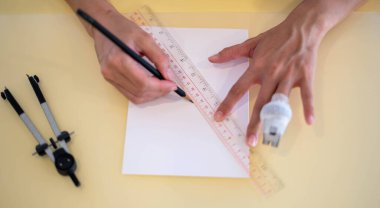The female hand using a ruler with the pencil prepares to draw and sketch on the empty white paper.