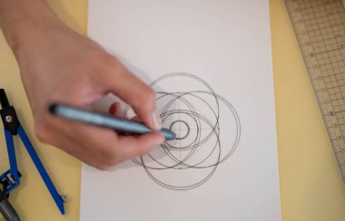 A female hand using a black magic pen preparing to draw and sketch the mandala concept on the empty white paper.