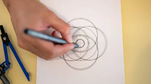 A female hand using a black magic pen preparing to draw and sketch the mandala concept on the empty white paper.