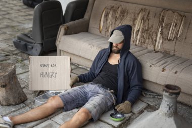 Şapkalı ve parmaksız eldivenli bir dilenci sokakta oturup para dileniyor.