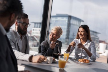 Bir grup iş adamı şirketin restoranında kahvaltı yapıyor. Ortadaki kadına odaklan.