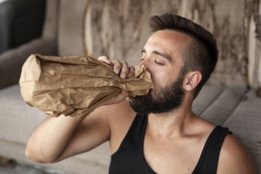 Sarhoş, binanın çatısındaki terasta oturmuş, elinde bir şişe kağıt torbayla içki içiyor.
