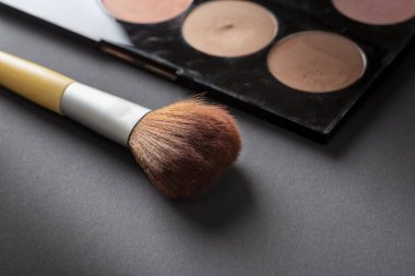 Yüz pudrası paletinin yüksek açısı ve siyah arkaplanda izole edilmiş bir makyaj fırçası.