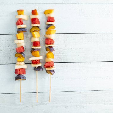 Yaz tatlısı olarak barbekü çubuklarında servis edilen soğuk renkli karışık meyve salatası tablosu.