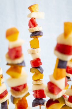 Barbekü çubuklarında servis edilen renkli karışık mevsimlik meyve salatası yaz partisi tatlısı olarak karpuza sıkışmış. Çerçevenin merkezindeki meyve çubuğuna odaklan.