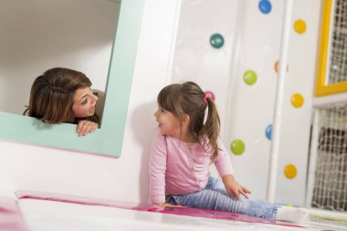 Anne ve kızı oyun odasında oynuyorlar, küçük tahta bir evde saklanıyorlar, saklambaç oynuyorlar.