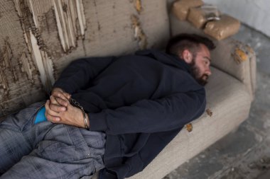 Kanepede kelepçeli halde tutuklu bir uyuşturucu satıcısı. Parmaklara ve kelepçelere odaklan.