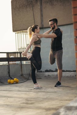 Çalışmadan önce terasta uzanan genç bir çift; arka planda kentsel ufuk çizgisi