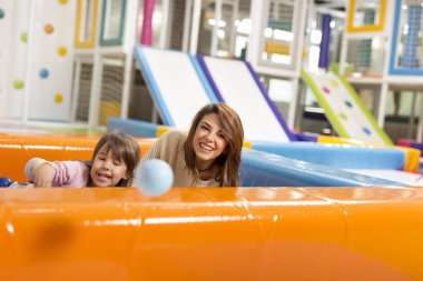 Neşeli anne ve kız renkli toplarla dolu bir havuzda oyun odasında oynuyorlar. Annesine odaklan.