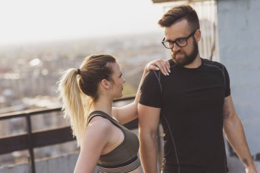 Çalışmadan önce terasta uzanan genç bir çift; arka planda kentsel ufuk çizgisi