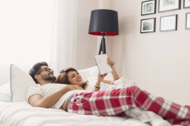 Birbirine aşık çiftler, yatakta yatıyorlar, tablet bilgisayarda internette dolaşıyorlar, haberleri okuyorlar.